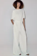 Pantalón wide leg de tiro medio, color blanco con diseño de rayas diplomáticas a contraste, bolsillos laterales y de vivo en la espalda, pinzas en el delantero y cierre frontal con cremallera, botón y ganchos metálicos.