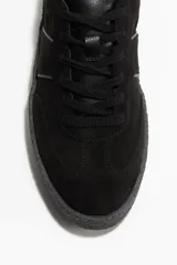 Zapatillas deportivas negras de gamuza con cuello acolchado, lengüeta, cierre de cordones y suela texturizada gruesa.