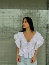 Blusa blanca con escote en V, mangas cortas con volados y lazos en el escote.
