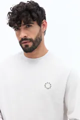 Remera de manga larga color blanco roto o gris muy claro, con escote redondo y un pequeño logo circular estampado en el pecho.