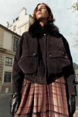 Chaqueta estilo bomber de corte oversize en color marrón oscuro, confeccionada con acabado aterciopelado. Presenta un cuello de solapa con detalle de pelo sintético desmontable, cierre frontal oculto con cremallera y botones a presión, bolsillos delanteros con solapa y bajo elástico.