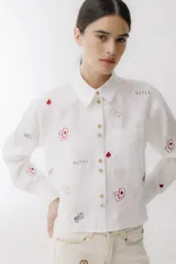 Camisa de lino blanca con cuello clásico, cierre frontal con botones dorados, bolsillo en el pecho y estampado de dados, cartas y picas.