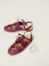 Sandalias planas tipo slingback de cuero marrón, con diseño delantero calado, cierre de cordones y tira trasera ajustable con hebilla.