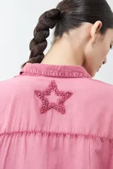 Camisa de corte clásico y manga larga en tono celeste claro, con diseño de estrellas aplicadas en tejido desflecado. Presenta cuello camisero y cierre frontal con botones.
