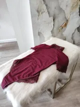 Body de lycra color bordó con cuello alto, mangas cortas y espalda descubierta. Presenta detalles de encaje en el cuello, mangas y laterales de la parte inferior. Cuenta con cierre de broches en la entrepierna.