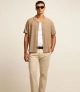 Pantalón de vestir color marrón, de corte slim y largo cropped. Confeccionado en tejido de algodón liso, con bolsillos laterales y traseros. Cierre frontal con botón y cremallera.