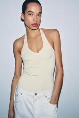 Top de cuello halter con diseño ajustado y escote con costuras tipo corset en el busto. Presenta espalda descubierta y bajo recto.