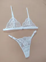 Conjunto de lencería de encaje blanco, compuesto por un corpiño triangular de tirantes regulables y una bombacha tipo colaless con tiras laterales ajustables.