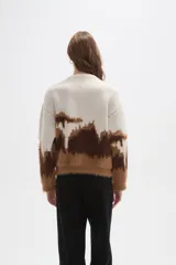 Sweater de punto con diseño de bloques de color en tonos crema, marrón oscuro y caramelo. Presenta una textura afelpada, cuello redondo a la base, mangas largas y corte holgado.