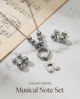 Set de joyería en acero quirúrgico compuesto por un collar con dije de nota musical y aros tipo bolita. El collar presenta una cadena con eslabones finos y una sección de esferas metálicas que conectan con un aro central del cual cuelga el dije. Los aros son de diseño minimalista en forma de esfera con cierre de presión.