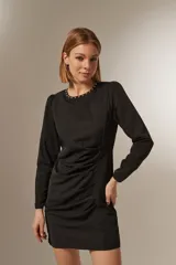 Minivestido negro de poliéster con mangas largas, cuello redondo con tachas plateadas, frunces laterales y corte ajustado.
