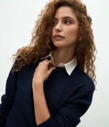 Suéter de punto gris con cuello redondo y diseño de cuello camisero celeste superpuesto. Presenta mangas largas y terminaciones acanaladas en puños y cintura.