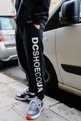 Pantalón de jogging DC Shoes modelo Clewiston, color negro con estampa vertical en contraste con el nombre de la marca en la pierna, puños elásticos en los tobillos y bolsillos laterales.