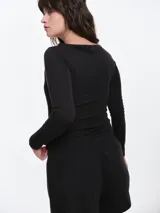 Remera de manga larga entallada en tejido pointelle, con escote bote y detalle de pequeño lazo central. Presenta un acabado con borde picot en el escote.