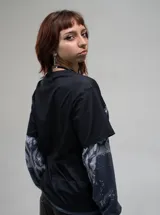 Remera de manga larga con diseño de doble capa, que combina una remera de manga corta negra con estampado gráfico gótico en el frente y mangas largas integradas con estampado abstracto en tonos grises.