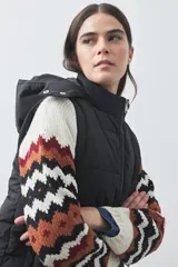 Chaleco puffer negro con diseño acolchado, capucha desmontable y cierre frontal. Cuenta con cordones ajustables en la cintura y bolsillos laterales.