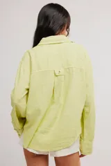 Blusa de lino color blanco crudo, de corte relajado, con cuello clásico, cierre frontal de botones, bolsillo en el pecho y mangas largas con presillas para arremangar.