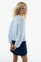 Blusa celeste a rayas blancas, de manga larga con elástico en los puños, escote en V y frente abierto con cierre de tiras para anudar.