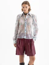 Camisa transparente de mesh rayado con bordados de dragones en verde y naranja. Tiene cuello clásico, botones negros forrados, puños de popelina y mangas abullonadas.