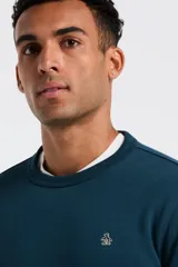 Buzo de cuello redondo en color azul petróleo, confeccionado en tejido de punto fino. Presenta puños y ruedo acanalados, con el logo de la marca bordado en el pecho.