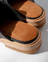 Mules de cuero negro con hebilla plateada y suela color madera.