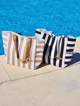 Bolso de playa tipo tote con diseño de rayas verticales, confeccionado en tela resistente con asas reforzadas y etiqueta decorativa en el frente.