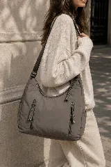 Cartera hobo gris de tela suave y liviana, con bolsillos frontales con cierre y tiradores trenzados, correa ajustable y compartimento principal con cierre.