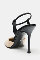 Zapato de tacón alto destalonado, fabricado en piel combinada en tonos beige y negro. Presenta punta redonda, tacón fino de 10 cm y tira elástica ajustable en el talón.