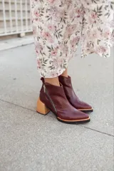 Bota corta de cuero color borgoña con textura de piel de reptil, cierre lateral con cremallera y tacón geométrico de madera clara.