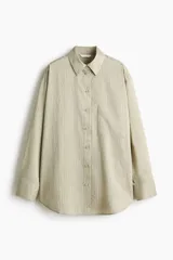 Camisa de corte oversized, color beige claro con rayas finas, cuello clásico, cierre frontal con botones, un bolsillo aplicado en el pecho, hombros caídos y mangas largas con puños abotonados.
