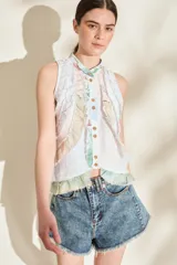 Top sin mangas de color blanco con estampado multicolor y detalles de volados desflecados, cuello mao y cierre frontal con botones.
