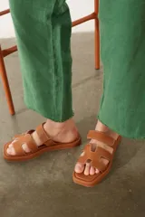 Sandalias planas de diseño minimalista en color tostado, con tiras anchas en forma de H y costuras a la vista. Poseen puntera cuadrada y suela plana.