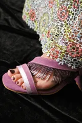 Sandalias de cuero marrón con tiras finas, cierre con hebilla y detalle de flecos con cuentas en el tobillo.