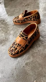 Mocasines de cuero en color dorado con detalles en marrón, con diseño bicolor y costuras artesanales expuestas en el empeine.