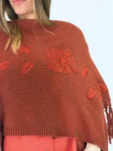 Ruana de algodón color crudo, tejida en punto abierto con detalles de flores bordadas en relieve y flecos en el borde inferior.