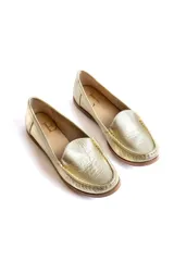 Mocasines de cuero color dorado con acabado texturizado, diseño clásico de punta redondeada y costuras visibles en el empeine. Cuentan con suela plana y flexible.