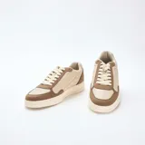 Zapatillas bajas de estilo retro, con paneles en color beige claro y marrón topo. Presentan cordones blancos y suela gruesa de color crema.