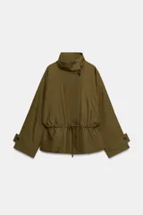 Parka amplia de Zara Woman Collection confeccionada en hilatura con mezcla de algodón, en color verde militar. Presenta cuello alto, manga larga con trabillas y botón, bolsillos laterales ocultos en costura, cintura ajustable con cordones y cierre frontal con botones.
