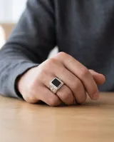 Anillo de acero tipo sello con piedra central rectangular color negro y diseño lateral grabado con motivo de flor de lis.