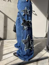 Pantalón jeans azul de corte wide leg, tiro medio y diseño holgado, con grandes aplicaciones de estrellas negras desgastadas en los laterales de las piernas.