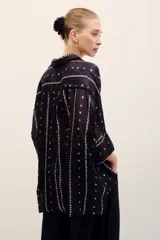 Camisa de seda negra con estampado geométrico de líneas verticales con rombos pequeños en tonos claros, cuello camisero, mangas largas con tajitos en los puños y cierre frontal con botones.