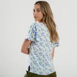 Blusa blanca con estampado de flores azules y verdes, cuello redondo con abertura en forma de gota y mangas cortas amplias.