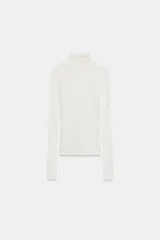 Camiseta blanca de cuello alto y manga larga con detalle de superposición de musculosa a tono. Presenta un corte entallado y está confeccionada con una mezcla que incluye lana.