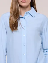 Camisa de calce relajado color celeste, confeccionada en tejido de textura suave y fluida. Presenta cuello camisero y abotonadura frontal, mangas largas con puño ancho y ruedo curvo.