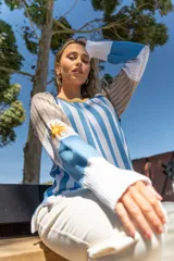 Sweater tejido a rayas verticales celestes y blancas, con cuello redondo amarillo y detalle bordado del sol de la bandera uruguaya en la manga.