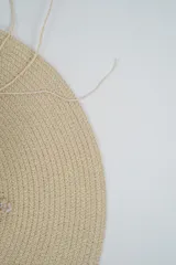 Sombrero de paja tejido color beige, de ala ancha y copa redonda, decorado con una sarta de caracoles marinos colgantes.