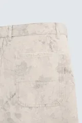 Bermuda de algodón color beige claro con efecto lavado y estampado abstracto en tonos grises. Diseño de corte relajado con cierre frontal de botón y cremallera, bolsillos delanteros y bolsillos traseros de plastrón.