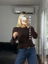 Saquito de tejido bremer color crema, con cuello redondo, cierre frontal de botones y detalles de volados en el ruedo y los puños.