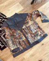 Camisa de manga larga con diseño combinado en tejido de jean azul y tela vintage con patrón geométrico multicolor en tonos azules, marrones y naranjas. Cuenta con cuello mao, cierre frontal con botones y puños ajustables con botones.