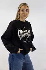 Buzo negro de cuello redondo y mangas largas, con estampa frontal en color blanco con la leyenda "DREAM BIG Start Small" y detalles de texto.